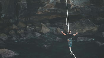 A tightrope walker on a rope over a dark canyon