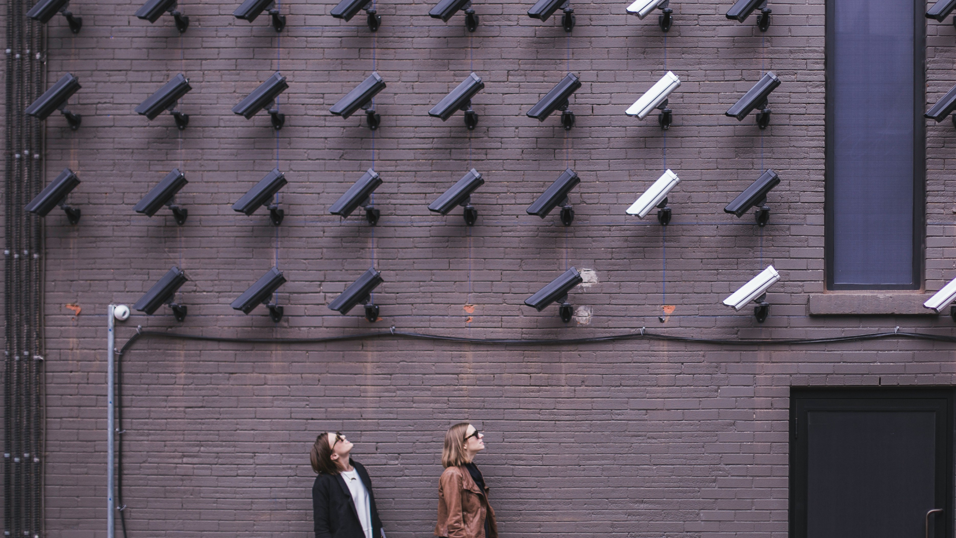 two people look up at a bank of security cameras